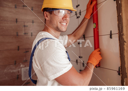 Cheerful male builder measuring ceramic wall tile 85961169