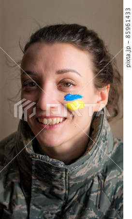 Indoor portrait of young girl with blue and yellow ukrainian flag on her cheek wearing military uniform, mandatory conscription in Ukraine, equality concepts Indoor portrait of young girl with blue and yellow ukrainian flag on her cheek wearing military uniform, mandatory conscription in Ukraine, equality concepts 85961433