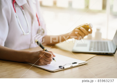 Female pharmacist holds a bottle of pills and a pen to write down the medical register on paper. Female pharmacist holds a bottle of pills and a pen to write down the medical register on paper. 85963237