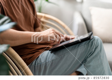 Technology Concept The male with his casual T-shirt and jeans sitting comfortably on the wooden chair and doing touchscreen for checking the web browser on the iPad 85972830