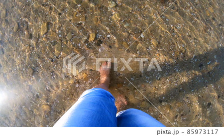 Girl walks barefoot on a sandy bottom with stones of the sea shore Girl walks barefoot on a sandy bottom with stones of the sea shore 85973117