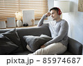 Pleasant young man listening to music on comfortable couch. 85974687