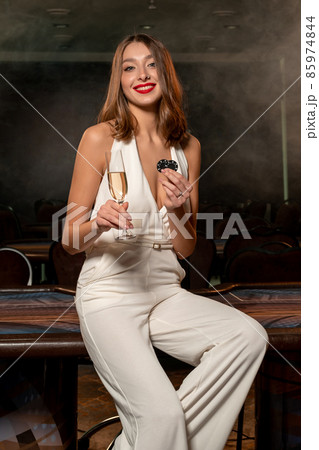 Smiling young woman with glass of champagne and betting chips near poker table Smiling young woman with glass of champagne and betting chips near poker table 85974844