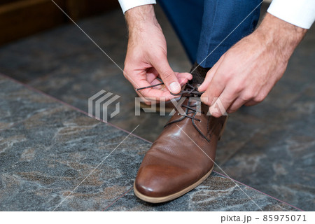 A young man ties the laces of his shoes - detail, selective fokus A young man ties the laces of his shoes - detail, selective fokus 85975071