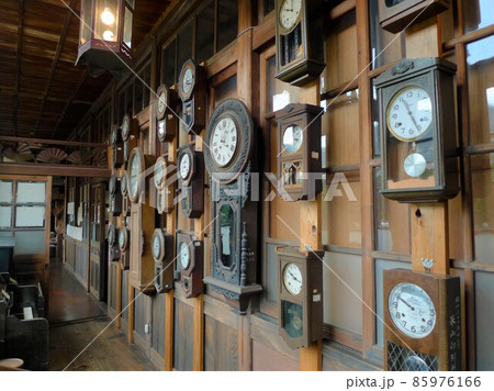 古い木造の建物の壁にかかるたくさんの古い時計、振り子時計