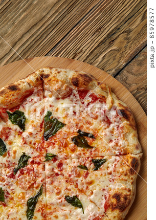 Uncut Italian pizza served with fresh basil leaf on Wooden board on dark texture background. Hot pizza with tomatoes and pesto sauce 85978577