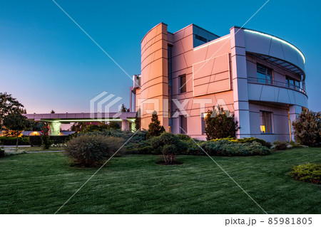 Manicured lawn, juniper plantations and flower beds around luxury mansion in summer evening 85981805