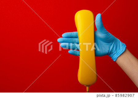 Female hand in medical glove holding yellow telephone speaker Female hand in medical glove holding yellow telephone speaker 85982907
