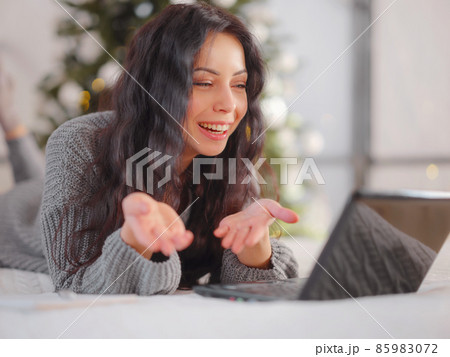 woman in cozy grey knitted sweater using laptop on bed , xmas holiday woman in cozy grey knitted sweater using laptop on bed , xmas holiday 85983072