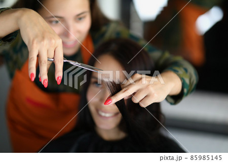 Concentrated professional hairdresser hold lock of hair and cutting with scissors 85985145