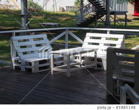 White bench and table from old wooden warehouse pallets stand on a wooden veranda in the park 85985198