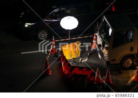 幹線道路の夜間工事 マンホール部分を照らす投光器と側方を通過する車 幹線道路の夜間工事 マンホール部分を照らす投光器と側方を通過する車 85986321