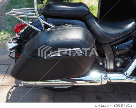 The back of a black motorcycle with a leather seat illuminated by sunlight 85987915