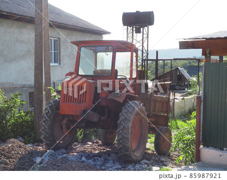An old red tractor stands on a broken path in a residential countryside 85987921