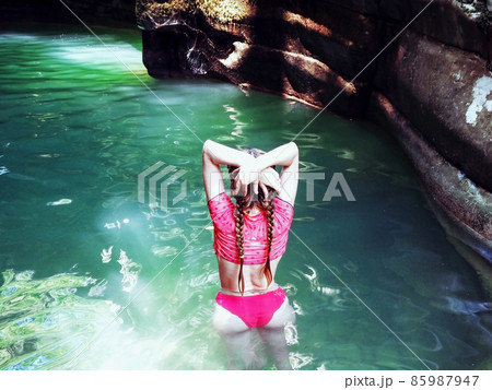 A girl with braids stands in a sun glare in the turquoise water flowing in a rocky gorge 85987947