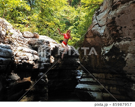 A girl in an orange swimsuit holding her nose with her hand flies from the canyon into the water A girl in an orange swimsuit holding her nose with her hand flies from the canyon into the water 85987957