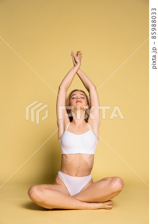 Studio shot of young adorable woman in underwear sitting on floor isolated over yellow background. Natural beauty concept. 85988033