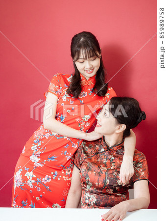 Mature asian mother hugging with her asian daughter on red background(Both wearing traditional cheongsam qipao). Mature asian mother hugging with her asian daughter on red background(Both wearing traditional cheongsam qipao). 85989758