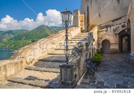 Watercolor drawing of Courtyard old medieval knight's castle on rock Castello Ruffo with stone ancient walls, street lamp, vases with flowers Watercolor drawing of Courtyard old medieval knight's castle on rock Castello Ruffo with stone ancient walls, street lamp, vases with flowers 85992818