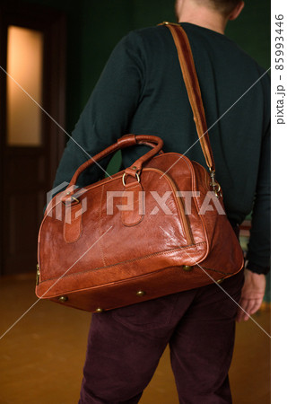 close-up photo of orange leather travel bag on mans shoulder 85993446