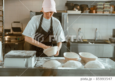 Serious woman spreads flour inside dish in contemporary bakery workshop 85993547