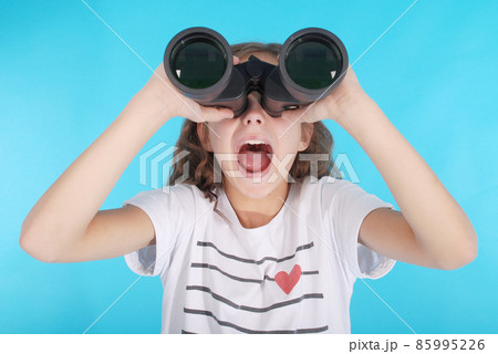 Beautiful young girl looking through binoculars with surprised expression Beautiful young girl looking through binoculars with surprised expression 85995226