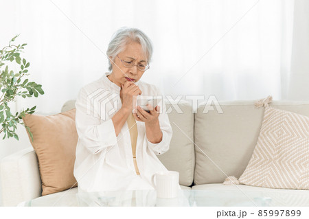 スマホを見る高齢者女性（悩む） 85997899