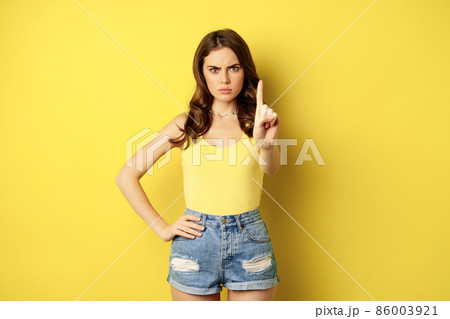 Serious stylish woman showing stop, rejection, prohibition gesture, decline something, disapprove, standing over yellow background 86003921