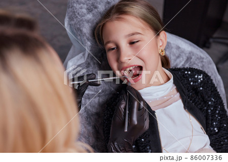 Caucasian young child girl sitting in medical chair while dentist fixing teeth at dental clinic using dental tools instruments, close-up photo of face. professional medical specialist. Caucasian young child girl sitting in medical chair while dentist fixing teeth at dental clinic using dental tools instruments, close-up photo of face. professional medical specialist. 86007336
