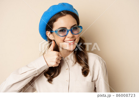 Image of happy smiling woman in stylish sunglasses, showing thumbs up in approval, recommending eyewear store, beige background Image of happy smiling woman in stylish sunglasses, showing thumbs up in approval, recommending eyewear store, beige background 86008723