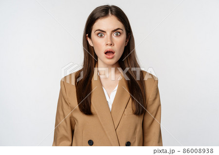 Portrait of shocked, speechless businesswoman gasping, staring stunned at camera, wearing brown suit, white background 86008938