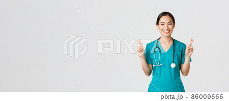Covid-19, healthcare workers, pandemic concept. Optimistic smiling asian female doctor, physician in scrubs having faith, cross fingers good luck, making wish, hope for better, white background Covid-19, healthcare workers, pandemic concept. Optimistic smiling asian female doctor, physician in scrubs having faith, cross fingers good luck, making wish, hope for better, white background 86009666