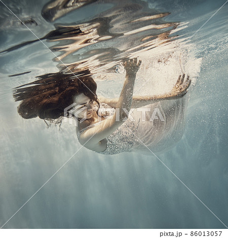 A girl in a white dress with dark hair swims underwater as if flying 86013057