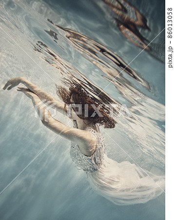 A girl in a white dress with dark hair swims underwater as if flying 86013058