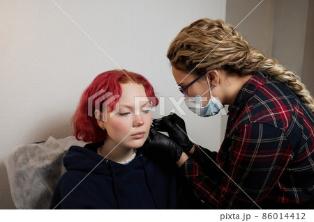 A beautician makes a puncture of the earlobe with a disposable device in a beauty salon. Ear piercing lobe. A beautician makes a puncture of the earlobe with a disposable device in a beauty salon. Ear piercing lobe. 86014412