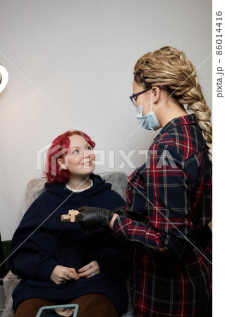 A beautician makes a puncture of the earlobe with a disposable device in a beauty salon. Ear piercing lobe. A beautician makes a puncture of the earlobe with a disposable device in a beauty salon. Ear piercing lobe. 86014416