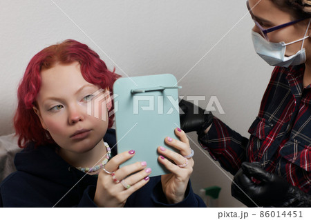 A beautician makes a puncture of the earlobe with a disposable device in a beauty salon. Ear piercing lobe. A beautician makes a puncture of the earlobe with a disposable device in a beauty salon. Ear piercing lobe. 86014451