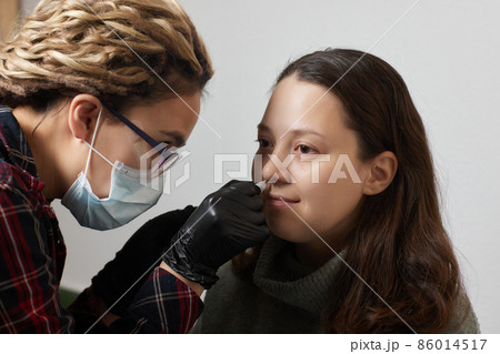 Closeup of a young woman's visage with piercing septum hanging from her nose. 86014517