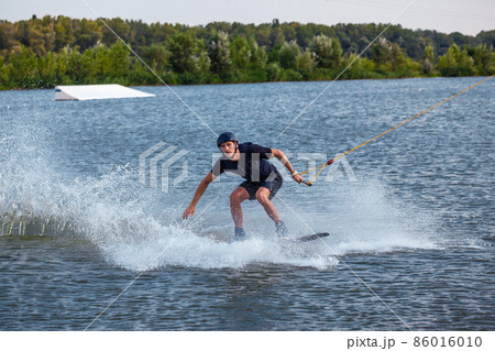 Man balancing on wakeboard towed on cable trying to make grab of board Man balancing on wakeboard towed on cable trying to make grab of board 86016010