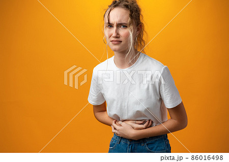 Sick young teen woman having a stomach ache against yellow background Sick young teen woman having a stomach ache against yellow background 86016498
