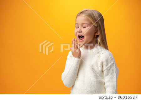 A tired little girl yawning against yellow background 86016527