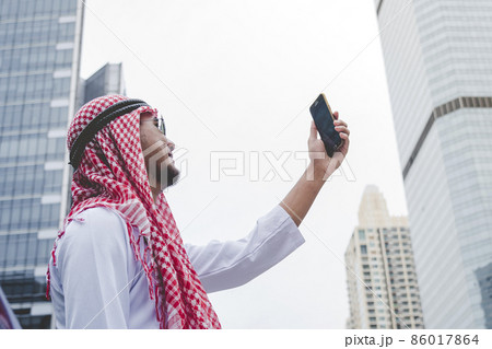 Islamic man using smartphones app organize schedule agenda  focus on hands holding smartphone muslim modern uae city. Arab men wear hijab and muslim formal dress sending text sms online lifestyle 86017864