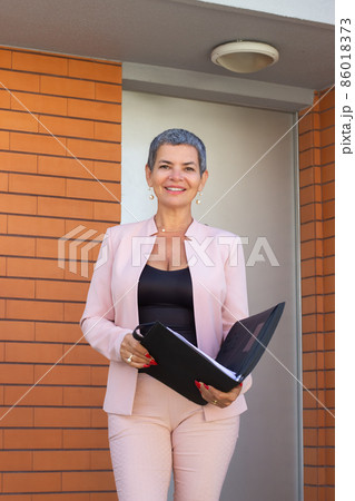Beautiful female real estate agent standing at house entrance Beautiful female real estate agent standing at house entrance 86018373