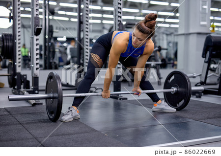 young female doing heavy duty squat in gym with barbell. Woman with perfect abs young female doing heavy duty squat in gym with barbell. Woman with perfect abs 86022669