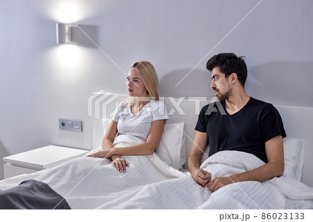 Irritated Caucasian Female And Male During Argue At Home, Sitting On Bed Together Irritated Caucasian Female And Male During Argue At Home, Sitting On Bed Together 86023133