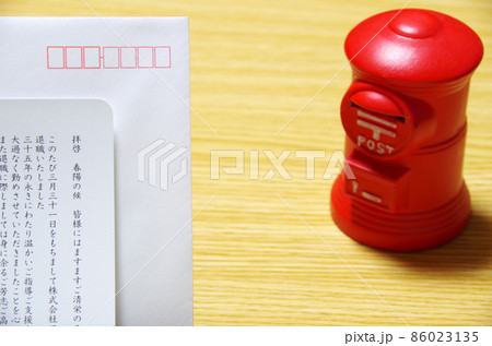 木目のテーブルに置いた郵便ポスト形の貯金箱と礼文の封筒 86023135