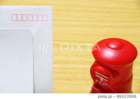 木目のテーブルに置いた郵便ポスト形の貯金箱と礼状の封筒（コピースペース有り） 86023906