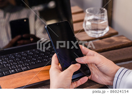ビジネス用　パソコン作業しながらスマホを打つ女性 86024154