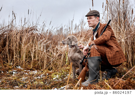 male hunter in suit clothes ready to hunt, holding gun and walking in forest. hunting and people male hunter in suit clothes ready to hunt, holding gun and walking in forest. hunting and people 86024197