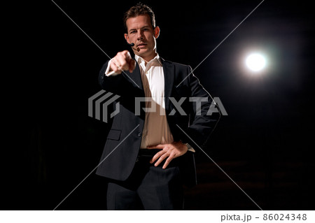 male speaker standing on stage and pointing finger to camera. projector in background male speaker standing on stage and pointing finger to camera. projector in background 86024348